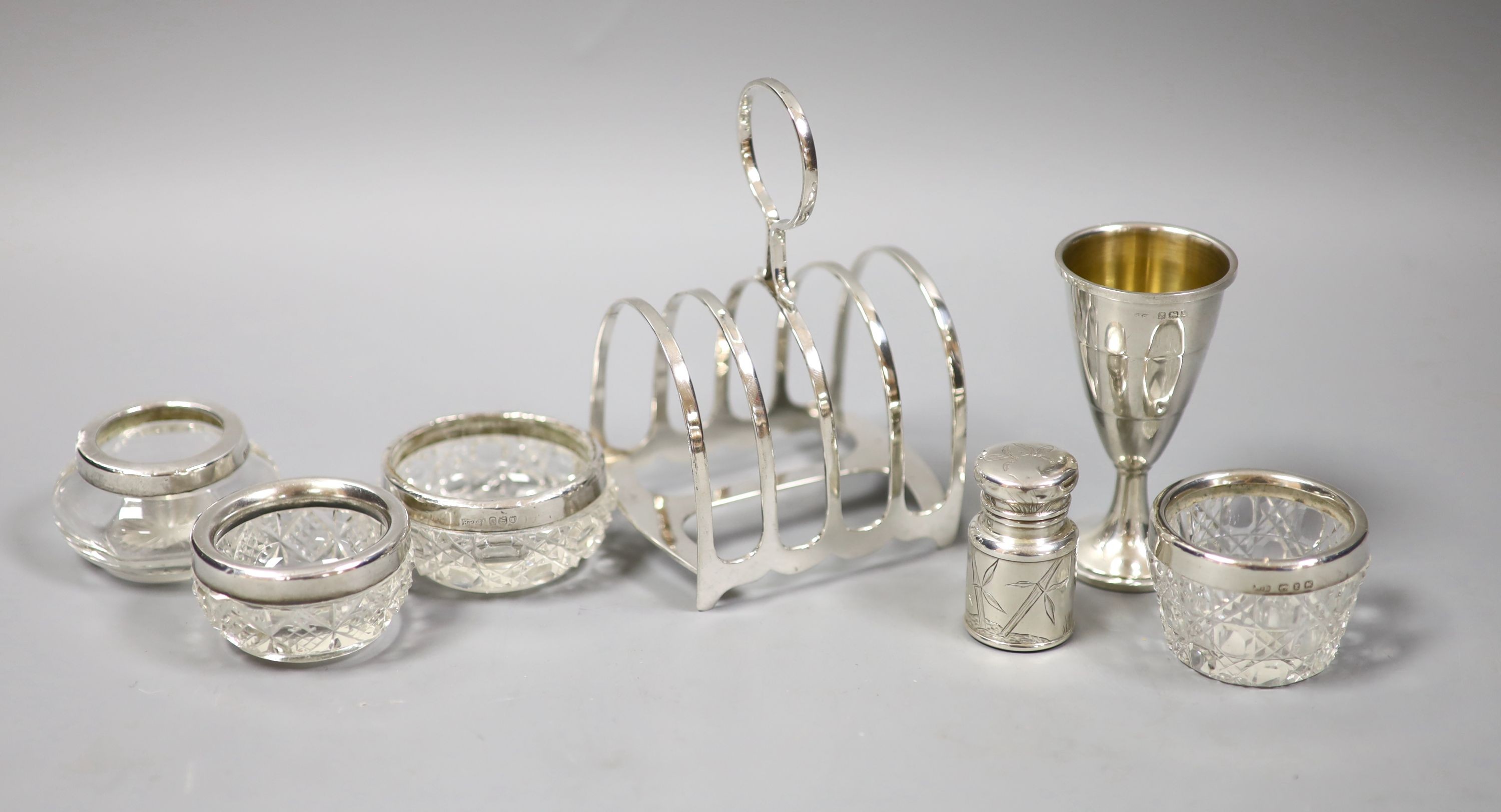 A silver toastrack, four silver mounted glass jars, a small silver goblet, and a Victorian silver scent bottle, London, 1883, 44mm.